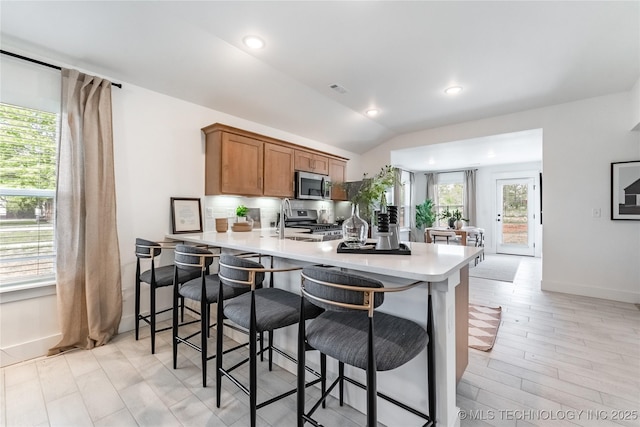 kitchen featuring lofted ceiling, stainless steel appliances, a peninsula, light countertops, and brown cabinetry