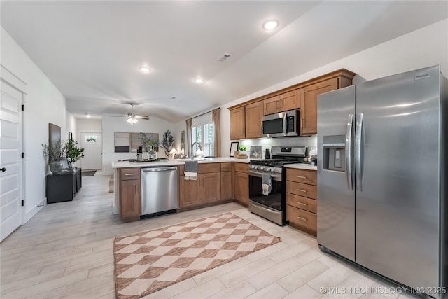 kitchen with a peninsula, open floor plan, light countertops, appliances with stainless steel finishes, and brown cabinetry