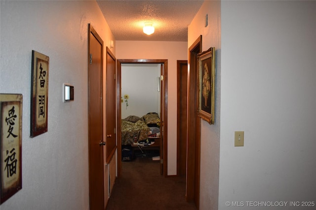 hall with dark colored carpet and a textured ceiling