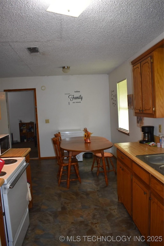 kitchen with white range with electric cooktop, light countertops, visible vents, brown cabinetry, and a sink