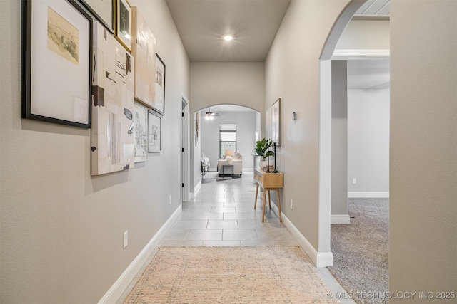 hallway with baseboards, arched walkways, and light tile patterned flooring