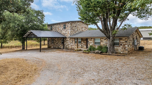 view of front of house with an attached carport, stone siding, central AC, and dirt driveway