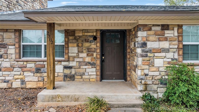 view of exterior entry with stone siding and a shingled roof