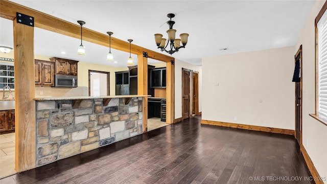 kitchen featuring a barn door, a peninsula, beam ceiling, dark wood-style floors, and stainless steel microwave