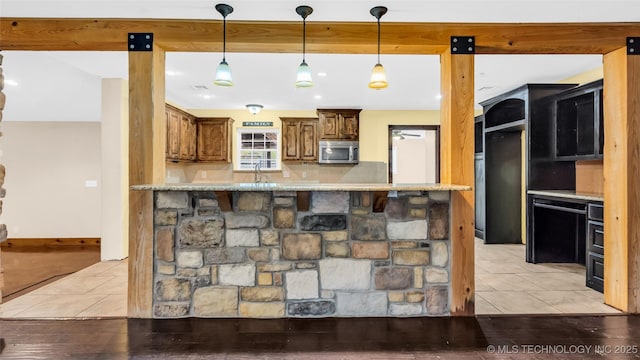 kitchen with light tile patterned floors, brown cabinetry, stainless steel microwave, a peninsula, and hanging light fixtures