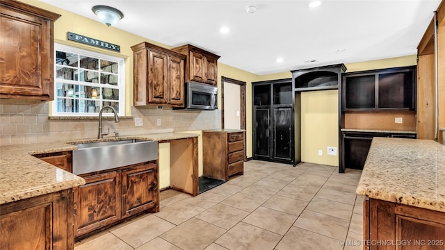 kitchen with decorative backsplash, light stone counters, stainless steel microwave, a sink, and light tile patterned flooring