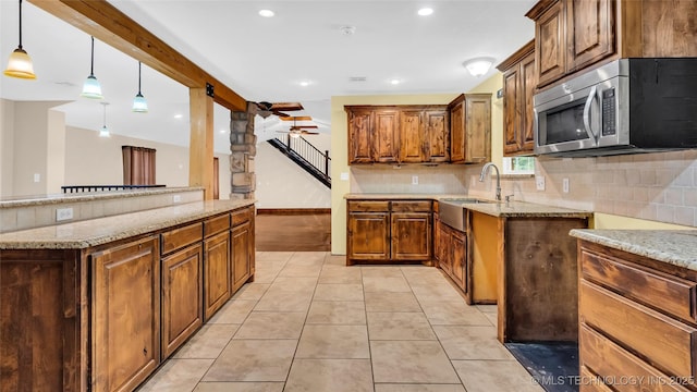 kitchen featuring light stone counters, pendant lighting, light tile patterned floors, stainless steel microwave, and a sink