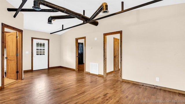 empty room featuring lofted ceiling, visible vents, baseboards, and wood finished floors