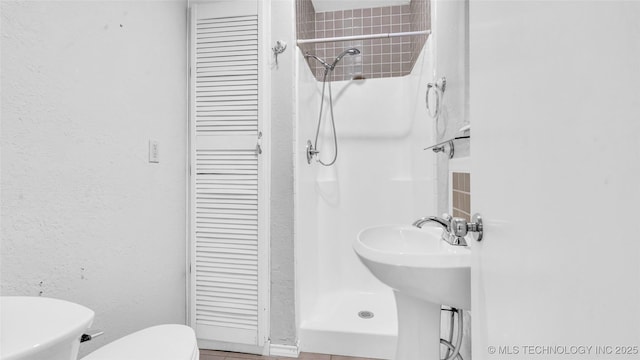 full bathroom featuring a closet, a textured wall, toilet, a shower stall, and a sink