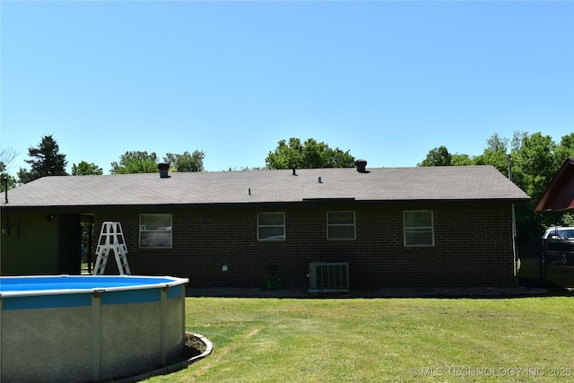 rear view of property with brick siding, a lawn, an outdoor pool, and central air condition unit