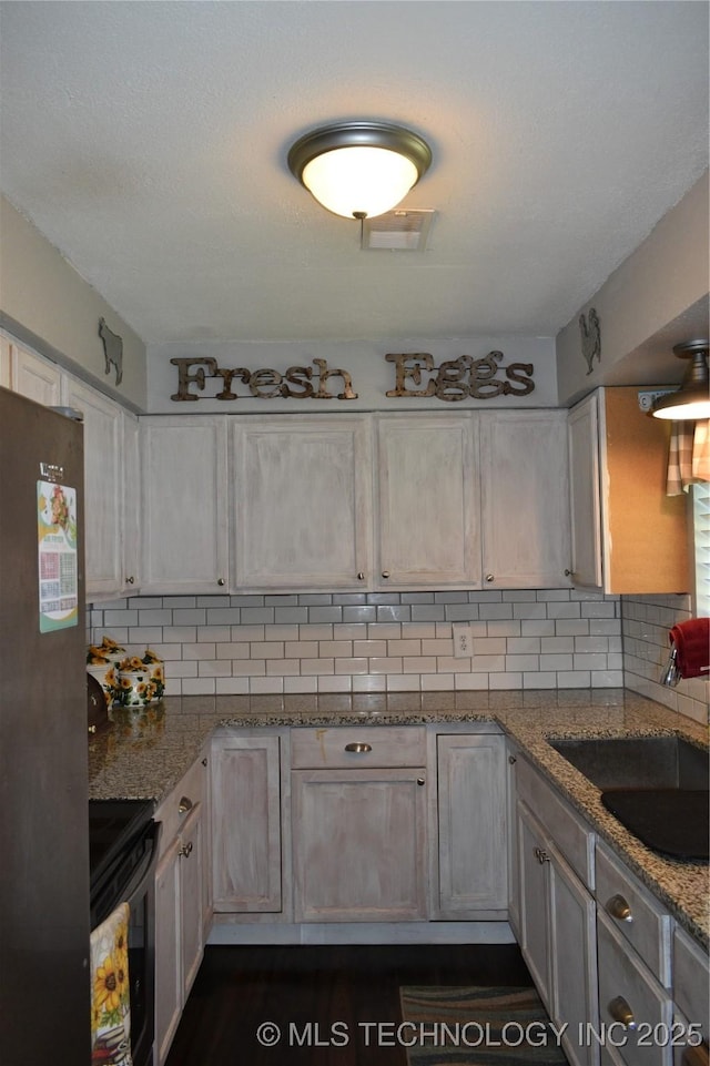 kitchen featuring range with electric stovetop, tasteful backsplash, visible vents, freestanding refrigerator, and a sink