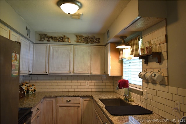 kitchen with light stone counters, range with electric cooktop, a sink, stainless steel refrigerator, and tasteful backsplash