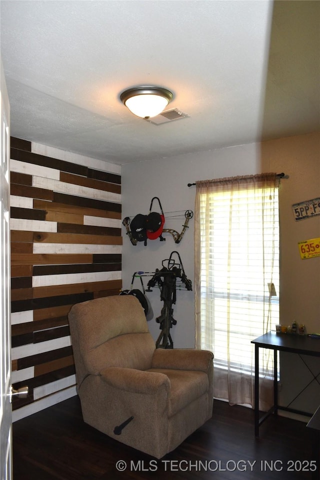 living area with dark wood-style flooring, visible vents, and wood walls