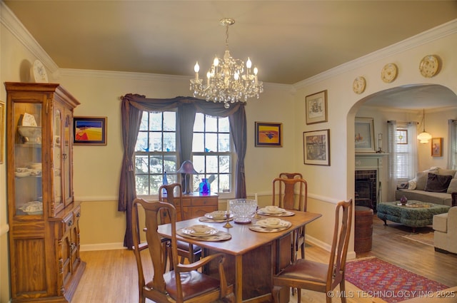 dining room with light wood-type flooring, baseboards, a fireplace, and ornamental molding