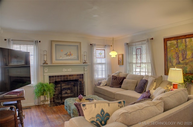 living room with wood finished floors, ornamental molding, plenty of natural light, and a tile fireplace