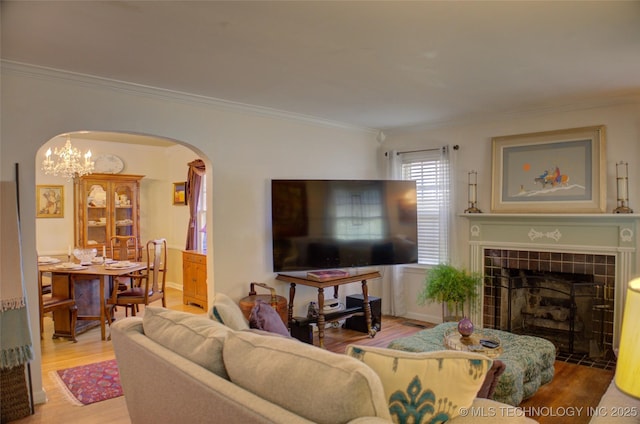 living area featuring arched walkways, ornamental molding, wood finished floors, a fireplace, and a chandelier