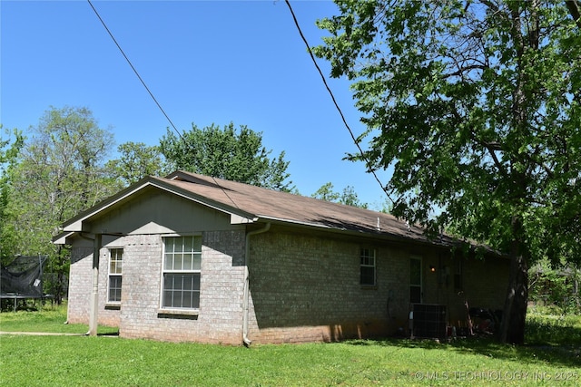 view of side of home with a trampoline, central AC, a lawn, and brick siding