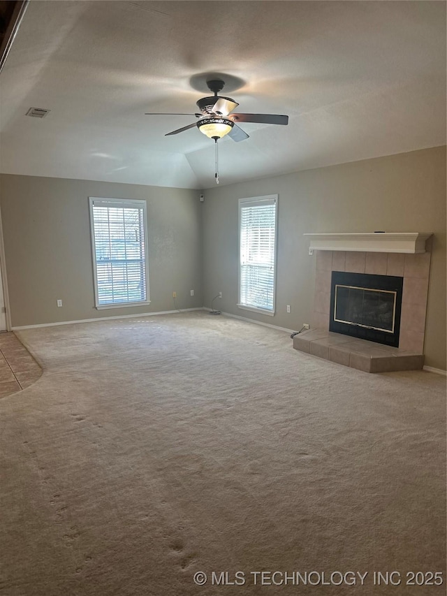 unfurnished living room featuring visible vents, lofted ceiling, carpet floors, a tile fireplace, and a ceiling fan