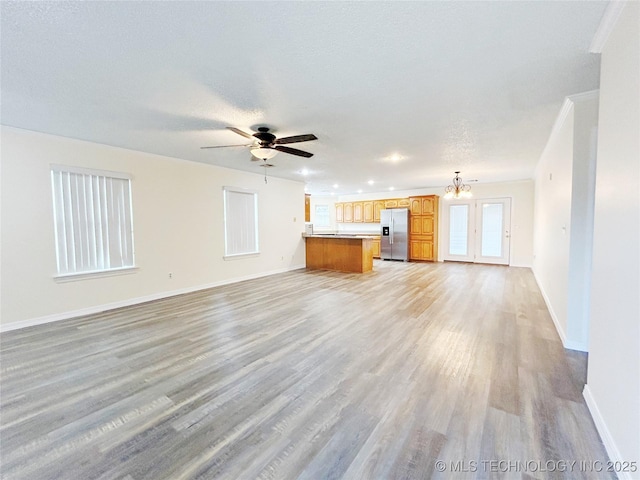 unfurnished living room with a textured ceiling, ceiling fan with notable chandelier, light wood-type flooring, and baseboards