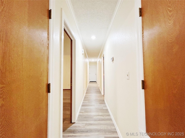 hallway with a textured ceiling, ornamental molding, light wood-type flooring, and baseboards