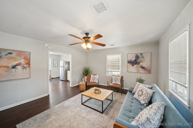 living area featuring a ceiling fan, visible vents, baseboards, and wood finished floors