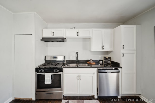 kitchen featuring white cabinets, dark countertops, stainless steel appliances, under cabinet range hood, and a sink