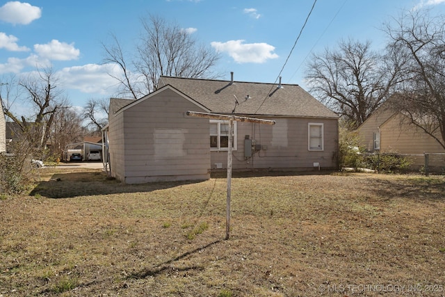 rear view of house with a shingled roof, fence, and a yard