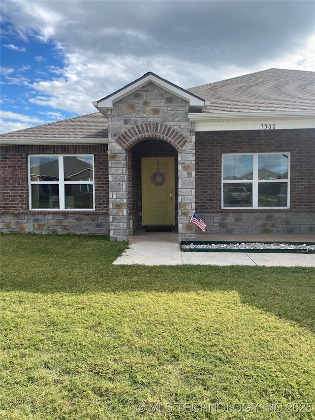 view of front of property with a front yard, roof with shingles, and brick siding