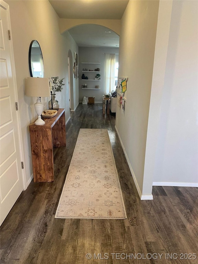 hallway with arched walkways, dark wood-type flooring, and baseboards