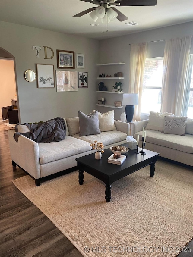 living area featuring a ceiling fan, arched walkways, visible vents, and wood finished floors