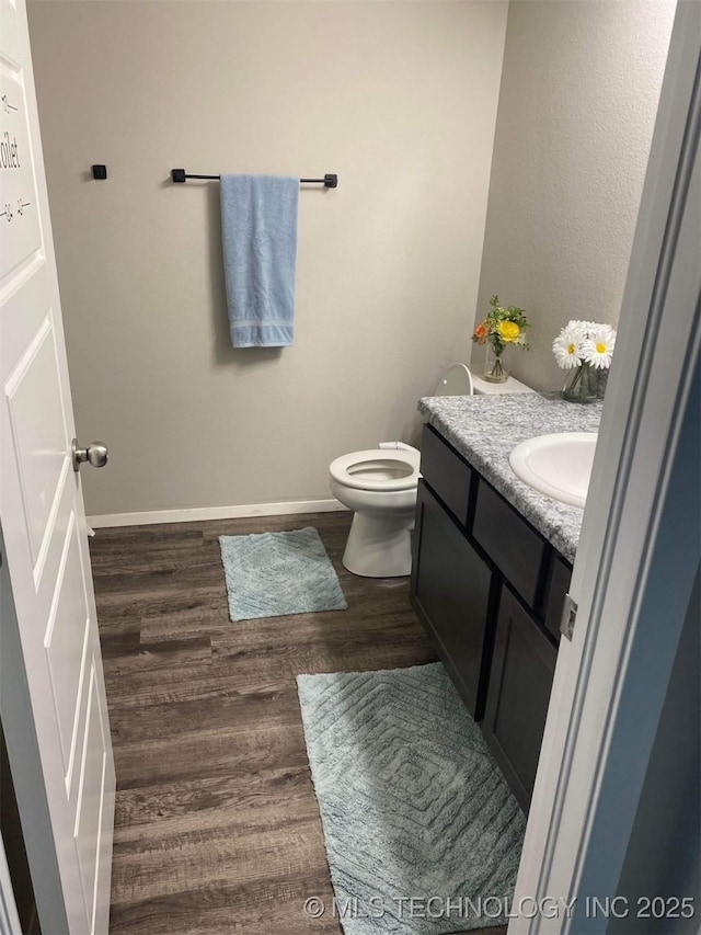 half bathroom featuring baseboards, vanity, toilet, and wood finished floors