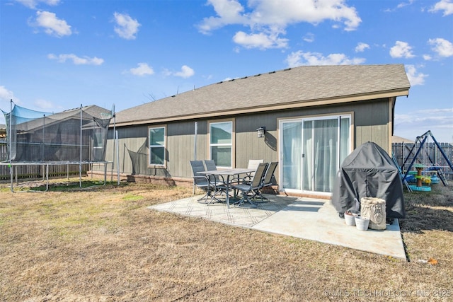 rear view of property featuring a patio, roof with shingles, a trampoline, fence, and a yard