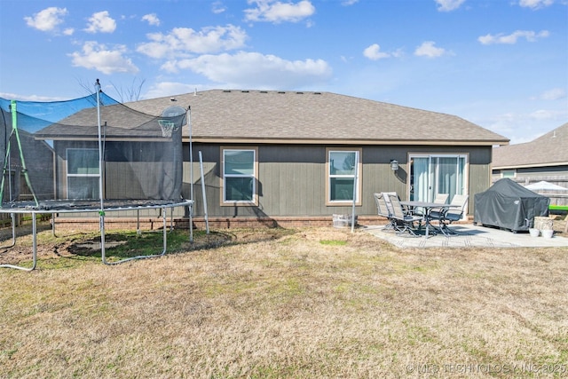 rear view of property with a trampoline, roof with shingles, a patio, and a lawn