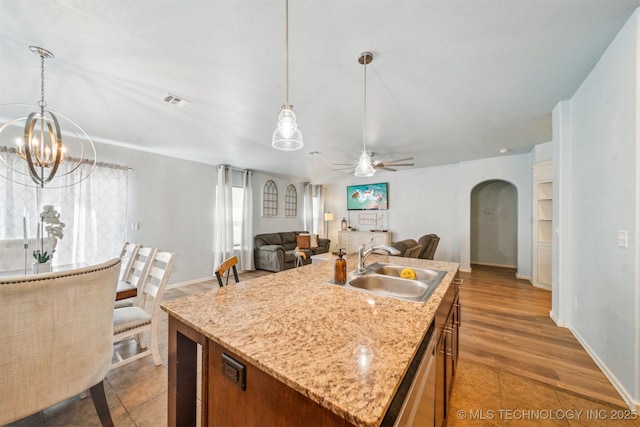 kitchen featuring arched walkways, decorative light fixtures, open floor plan, a sink, and an island with sink