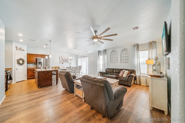 living area featuring light wood-style flooring, a textured ceiling, visible vents, and a ceiling fan