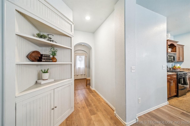 hallway featuring light wood-type flooring, arched walkways, and baseboards