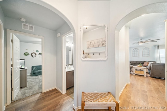 hall with light wood-style floors, baseboards, visible vents, and arched walkways