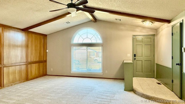 empty room featuring vaulted ceiling with beams, light colored carpet, visible vents, ceiling fan, and a textured ceiling