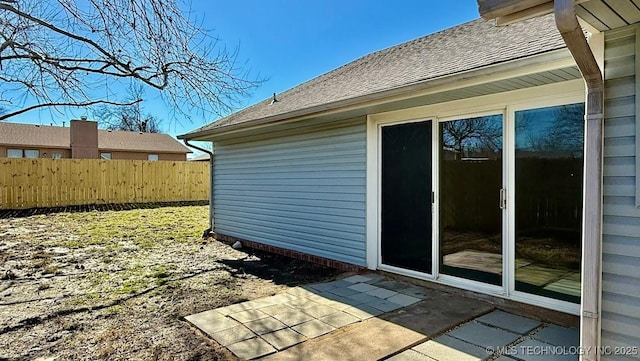 view of side of home featuring a shingled roof, fence, and a patio