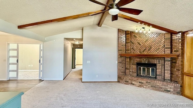 unfurnished living room featuring a textured ceiling, ceiling fan, lofted ceiling with beams, a fireplace, and carpet flooring