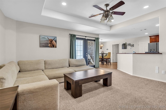 living room featuring light carpet, baseboards, ceiling fan, a tray ceiling, and recessed lighting