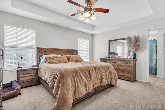 bedroom featuring baseboards, a tray ceiling, a ceiling fan, and light colored carpet