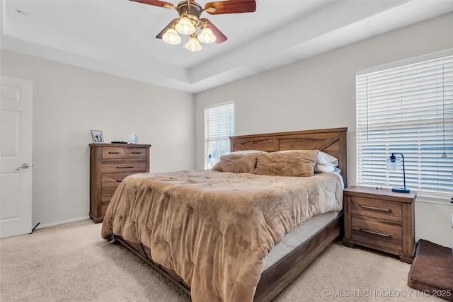 bedroom featuring a ceiling fan, a raised ceiling, light colored carpet, and baseboards