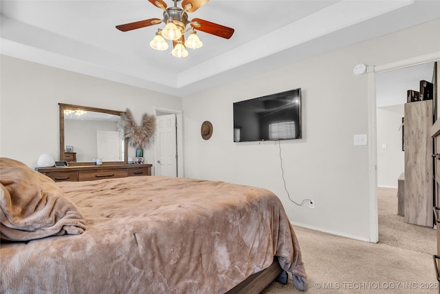 bedroom featuring light carpet, baseboards, a tray ceiling, and a ceiling fan