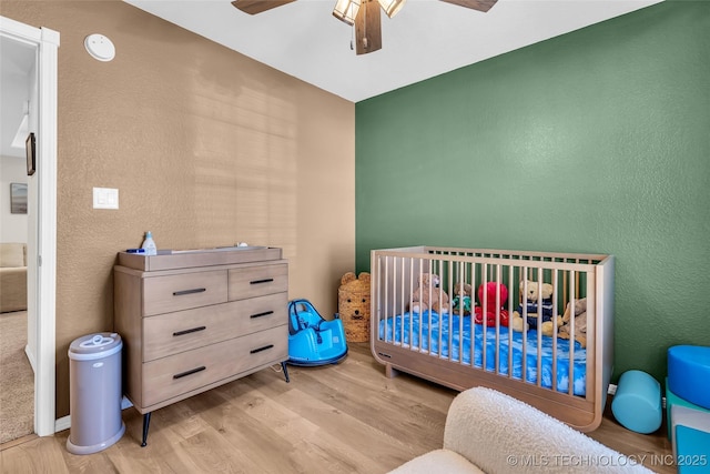 bedroom featuring ceiling fan, a crib, and light wood-style floors