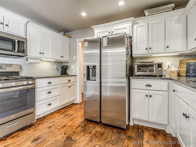 kitchen featuring stainless steel appliances, dark wood-style flooring, dark stone countertops, and white cabinets