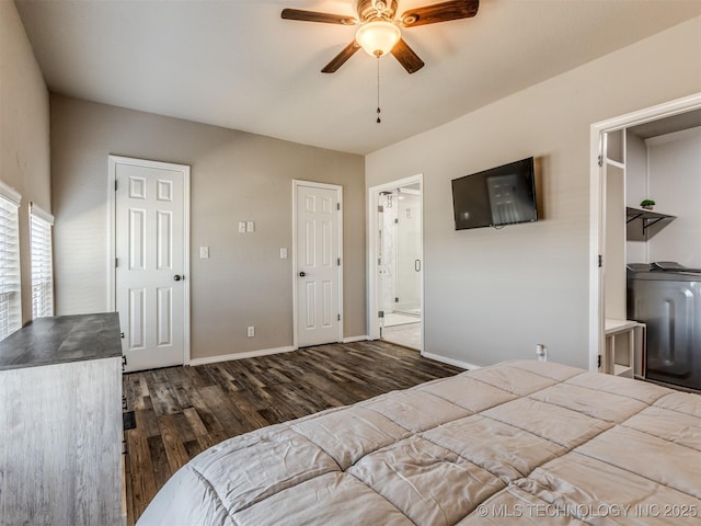 bedroom featuring dark wood finished floors, a ceiling fan, baseboards, ensuite bath, and washer / dryer