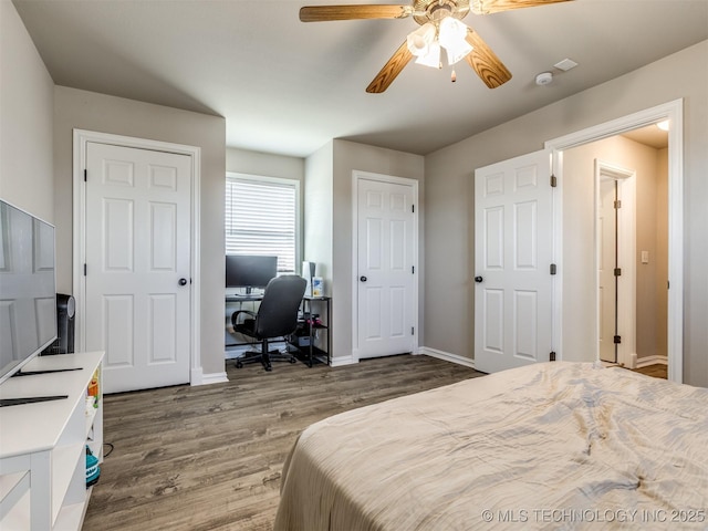 bedroom with two closets, ceiling fan, baseboards, and wood finished floors