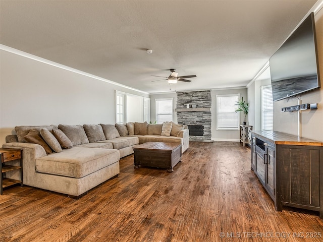 living room with ornamental molding, ceiling fan, a stone fireplace, and dark wood-type flooring