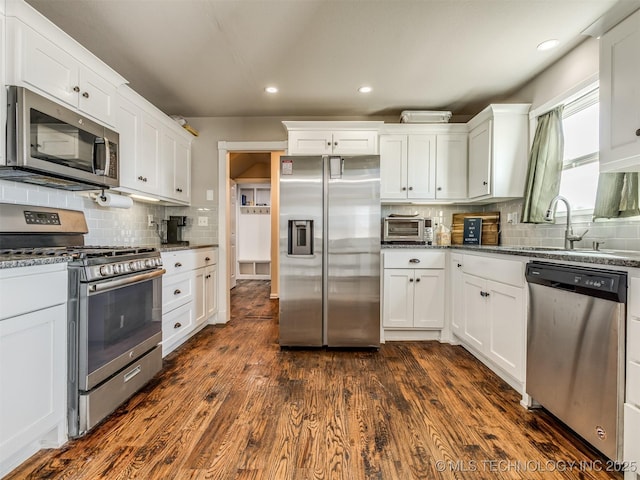 kitchen featuring stainless steel appliances, dark stone countertops, a sink, and white cabinetry